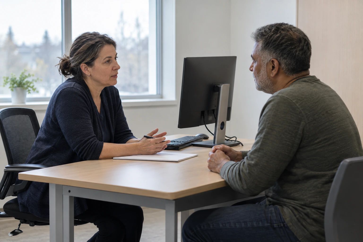 Two adults talking across a desk in a consultation room.